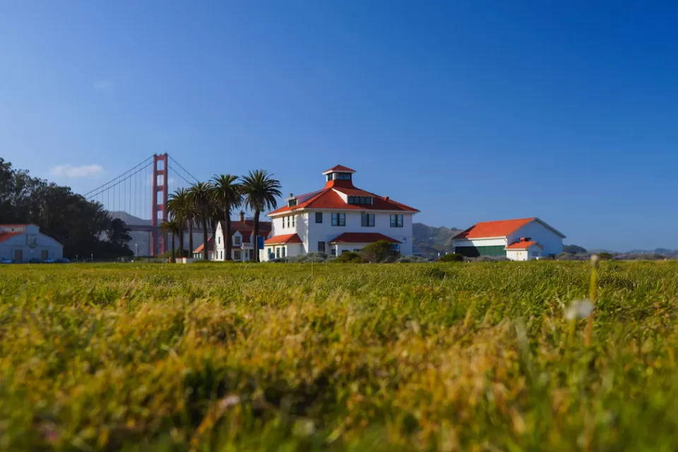 Green lawn with historic buildings and Golden Gate Bridge in background in Presidio national park site in San Francisco, California.